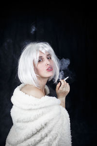 Portrait of female model smoking cigarette against black background