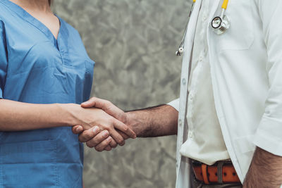 Midsection of doctor and patient shaking hands at clinic