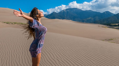 Young woman standing on sand at desert against sky
