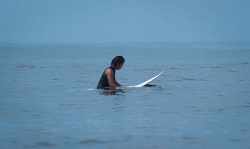 Side view of woman sitting on surfboard in sea