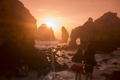 Rear view of people standing on rock at sunset