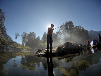 Rear view of man standing by lake against sky