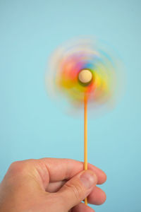 Close-up of hand holding pinwheel toy over blue background