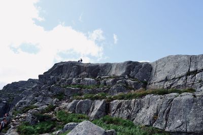 Low angle view of people on rock formation against sky