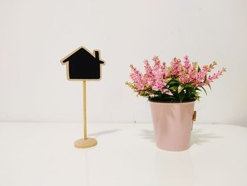 Close-up of flower pot by blackboard on table against wall