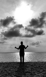 Silhouette man standing at beach against cloudy sky during sunset