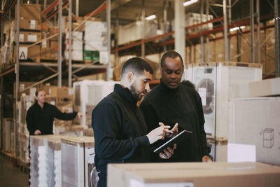 Male manual workers discussing over digital tablet at warehouse