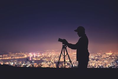 Silhouette man photographing cityscape against sky