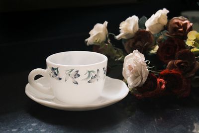 Empty cup by wilted roses on table