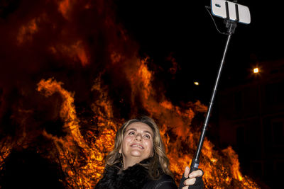 Woman taking selfie against bonfire at night