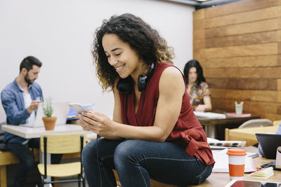 Young woman using phone while sitting on table