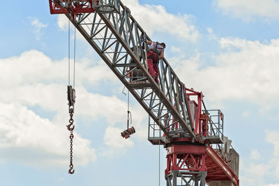 Low angle view of man standing crane against cloudy sky