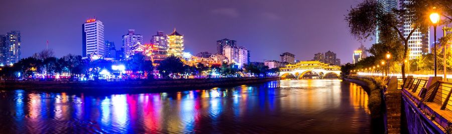 Panoramic shot of illuminated city by canal against sky at night