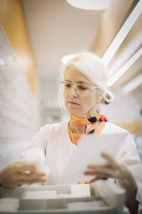 Mature female owner checking medicine by drawer in pharmacy store