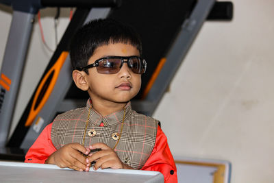 Cute boy wearing sunglasses looking away while standing against wall