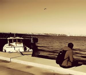 Rear view of man sitting at beach against clear sky