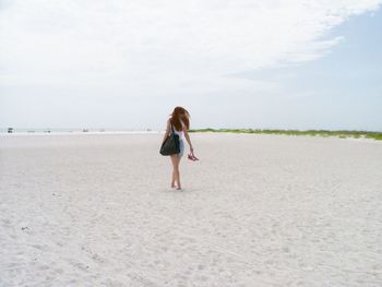 Rear view of woman walking at beach against sky