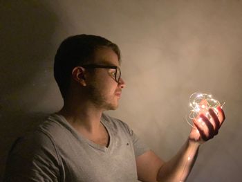 Close-up of young man holding illuminated string lights against wall