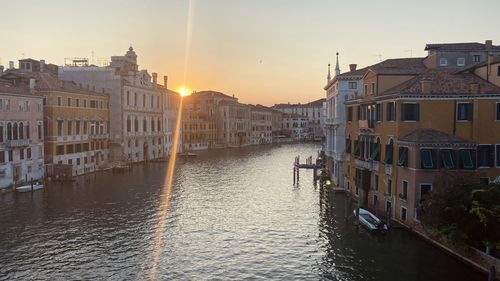 Canal amidst buildings in city during sunset