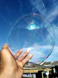 Cropped image of person holding bubbles against sky