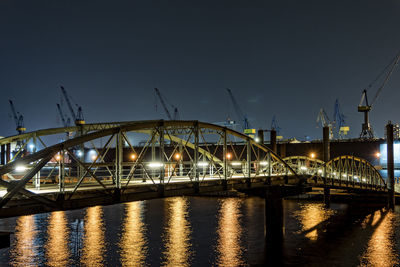 Illuminated bridge over river against sky at night