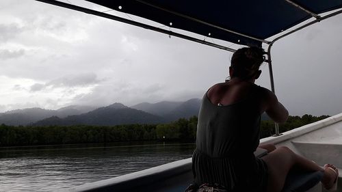 Rear view of woman sitting by lake against sky