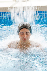 Young beautiful girl eyes closed, relaxing under a waterfall in a spa person