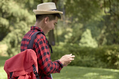 Side view of man wearing hat standing against trees
