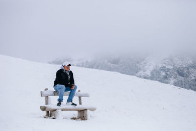 Man sitting on snowy bench during winter