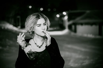 Close-up of young woman smoking cigarette while holding alcohol bottle at night