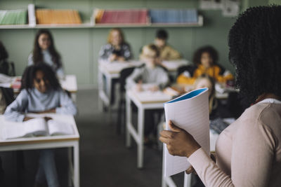 Side view of teacher showing notebook to students while teaching in classroom