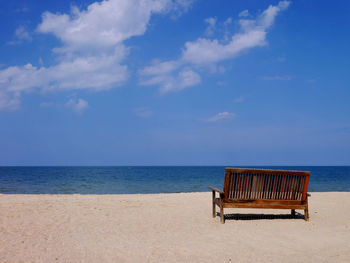 Empty bench on beach against sky