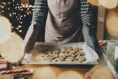 Woman holds deco, holding sheet with ready-made baked gingerbread cookies in her gloves hands