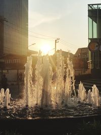 Fountain in city against sky during sunset