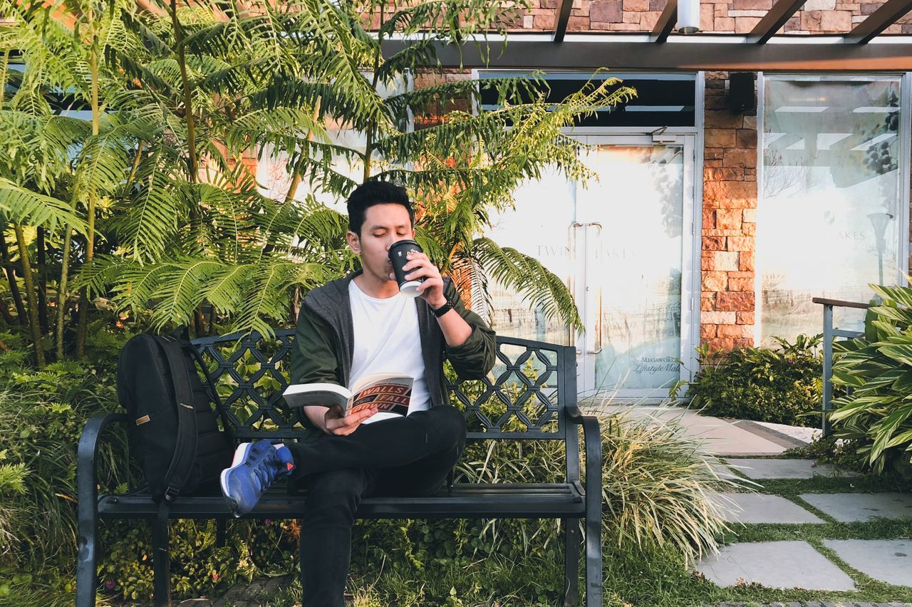 FULL LENGTH OF YOUNG MAN PHOTOGRAPHING WHILE SITTING ON PLANT