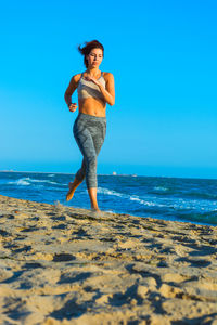 Full length of woman standing on beach against clear blue sky