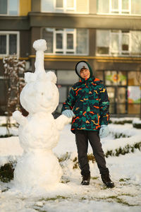 Winter portrait of a boy with a plastic sled sliding on a snowy slope and making a snowman