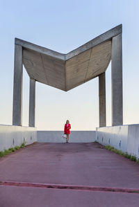 Woman standing on footpath below built structure