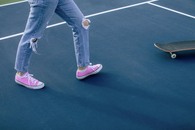 Low section of woman walking towards  skateboard