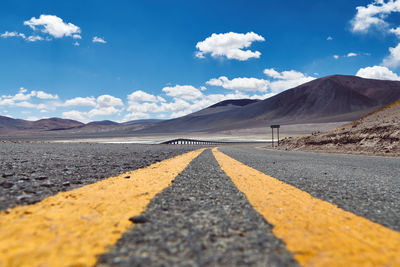 Surface level shot of country road by mountains against sky