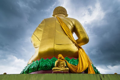 Low angle view of buddha statue against cloudy sky