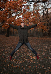 Full length of happy teenage boy jumping while screaming in park during autumn