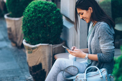 Smiling young woman using mobile phone in city