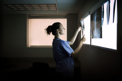 Rear view of woman looking through window at home