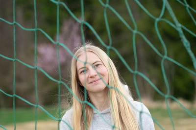 Portrait of young woman standing against chainlink fence