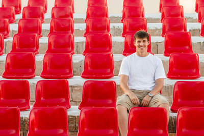 Wide smiling man  is sitting in deserted audience with red seats. absence of people 