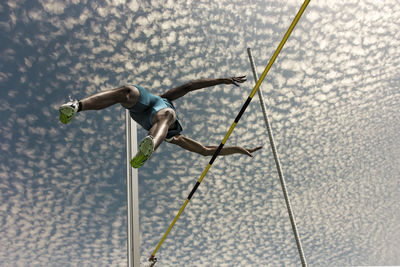 Low angle view of male athlete high jumping against sky