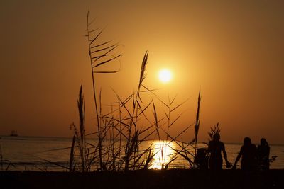 Silhouette people by sea against sky during sunset