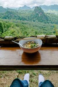 Low section of person with food on table in front of forest