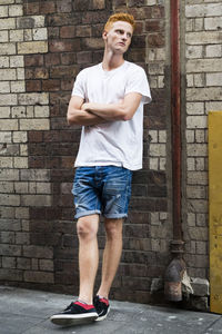 Full length portrait of man standing against brick wall
